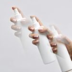 Multi-exposure shot of a hand with manicured nails holding a white spray bottle with a motion blur effect.
